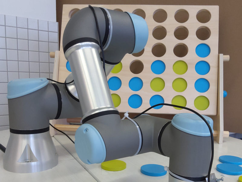 Roboterarm hebt ein Spielplättchen vor der Spieltafel auf